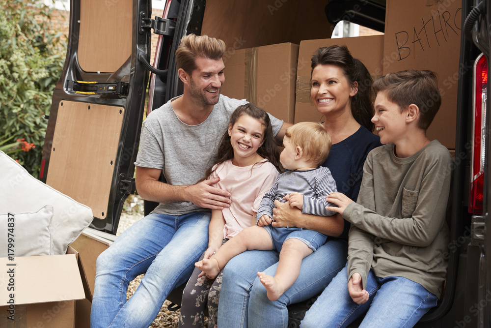Family Sitting In Back Of Removal Truck On Moving Day