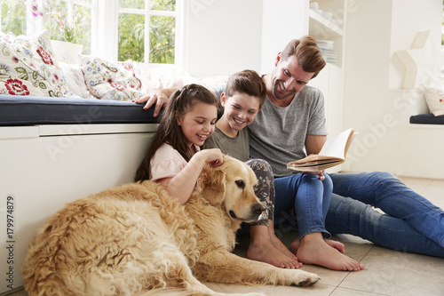 Father Reading Book With Son And Daughter And Pet Dog At Home