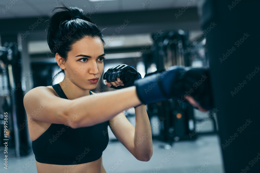 Side view of strong attractive brunette woman punching a bag with kickboxing gloves in the gym workout. Sport, fitness, lifestyle and people concept.