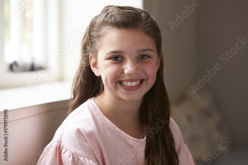 Portrait Of Smiling Young Girl Sitting On Window Seat At Home