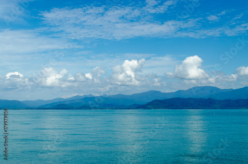 Horizontal of Seascape including Forest Mountain, Blue Sky and Wave of Water Foam in Ocean.