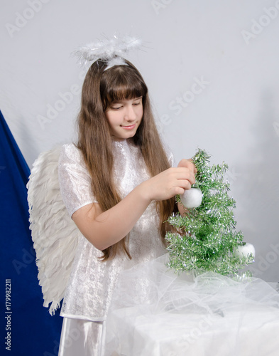 a girl in an angel costume decorates a Christmas tree photo