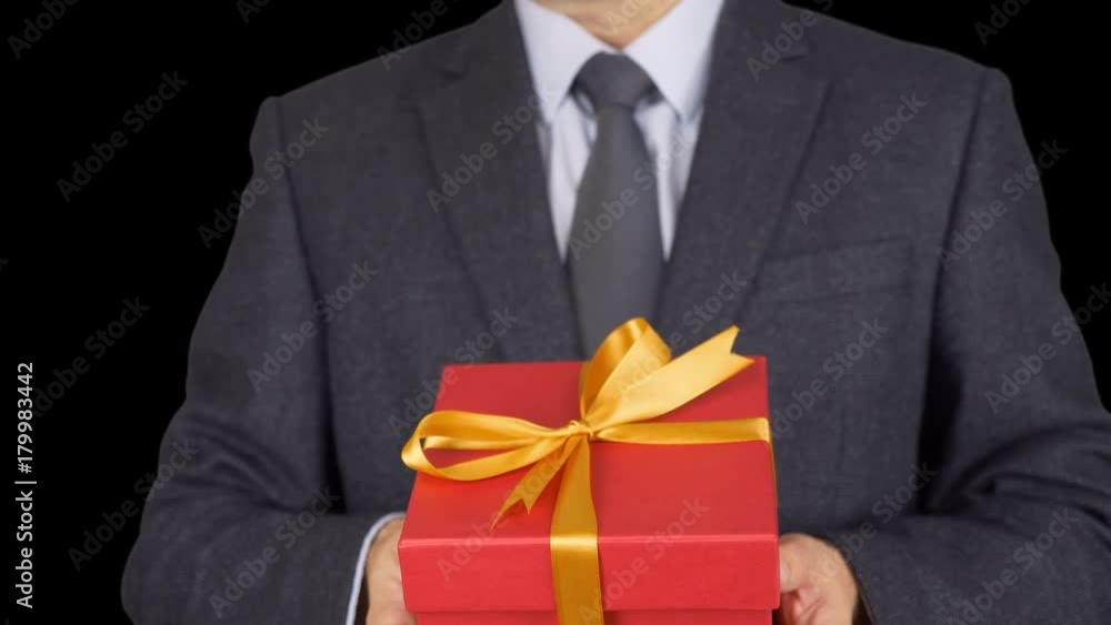 A man in a business suit with a tie is holding a red gift box. A man