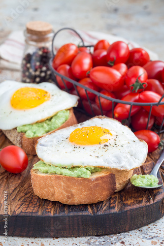Open sandwich with mashed avocado and fried egg on toasted bread, sprinkled with black pepper, vertical