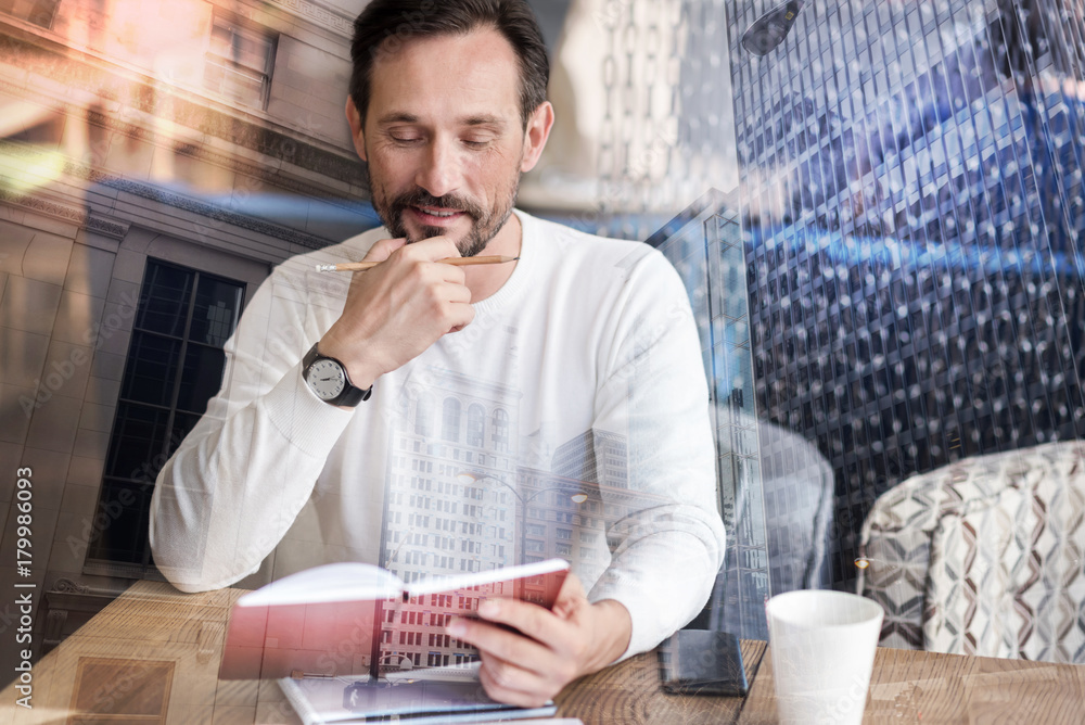 Planning the day. Handsome young man sitting at the table in the coffee house and revising his notes, being ready to make any corrections Planning the day. Handsome young man sitting at the table in the coffee house and revising his notes, being ready to make any corrections