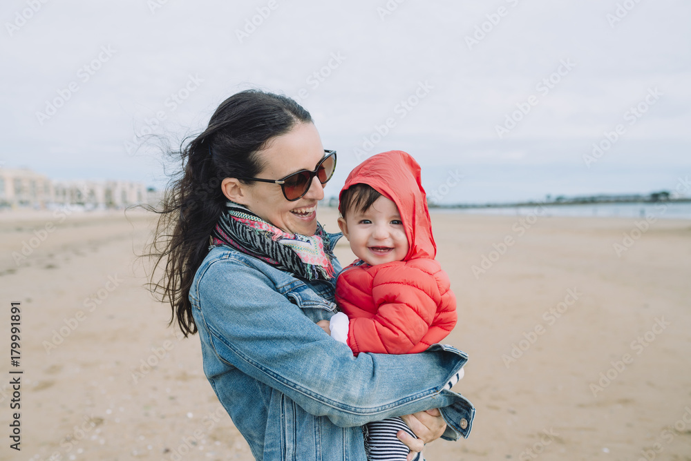 Portrait of smiling baby girl on her mother's arms on the beach