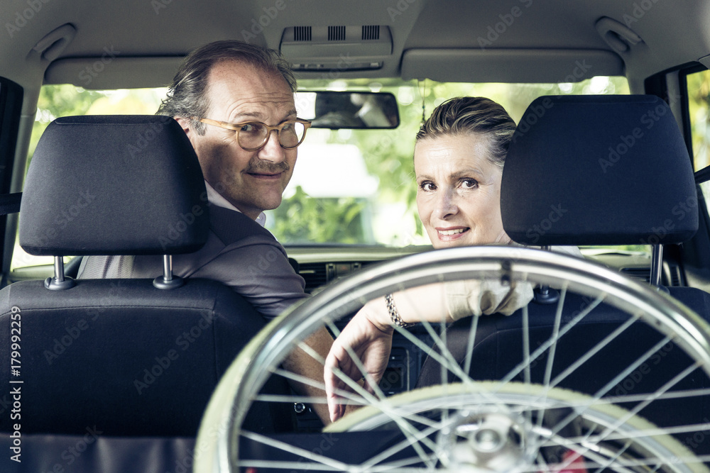 Smiling couple in car with wheelchair in boot