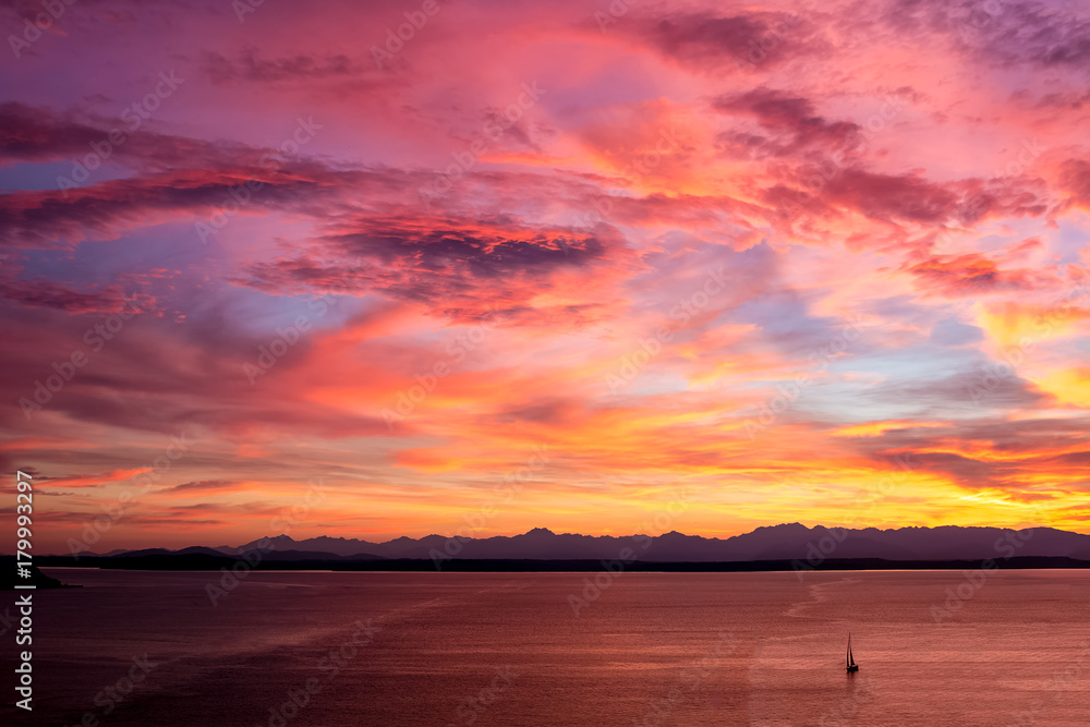 Red Yellow Orange Sunset On Water With Clouds of Same Colors Mountains in Background