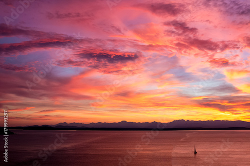 Red Yellow Orange Sunset On Water With Clouds of Same Colors Mountains in Background