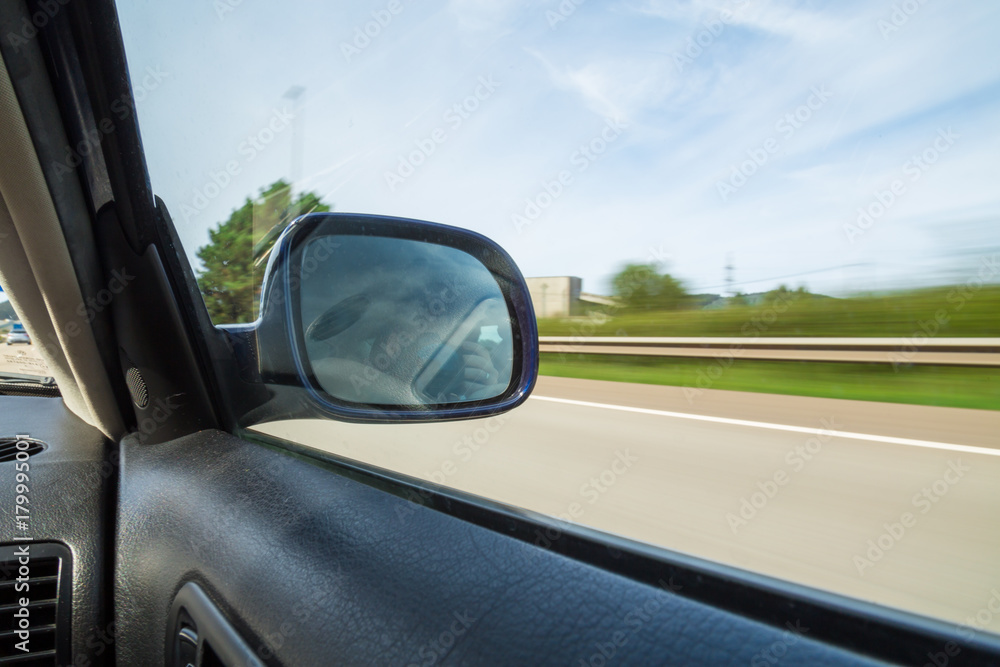 Rear view mirror of a car driving on a mountain road. 