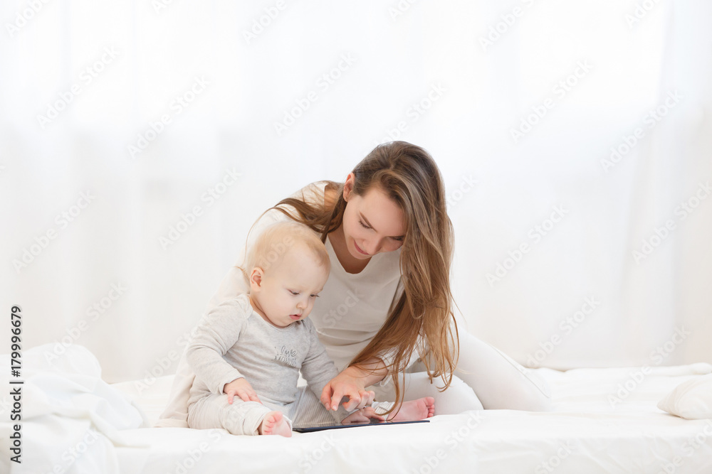 happy young mother plays the tablet with her little baby boy in a light drawing room at home. Education of the child on the tablet, a family portrait happy young mother plays the tablet with her little baby boy in a light drawing room at home. Education of the child on the tablet, a family portrait
