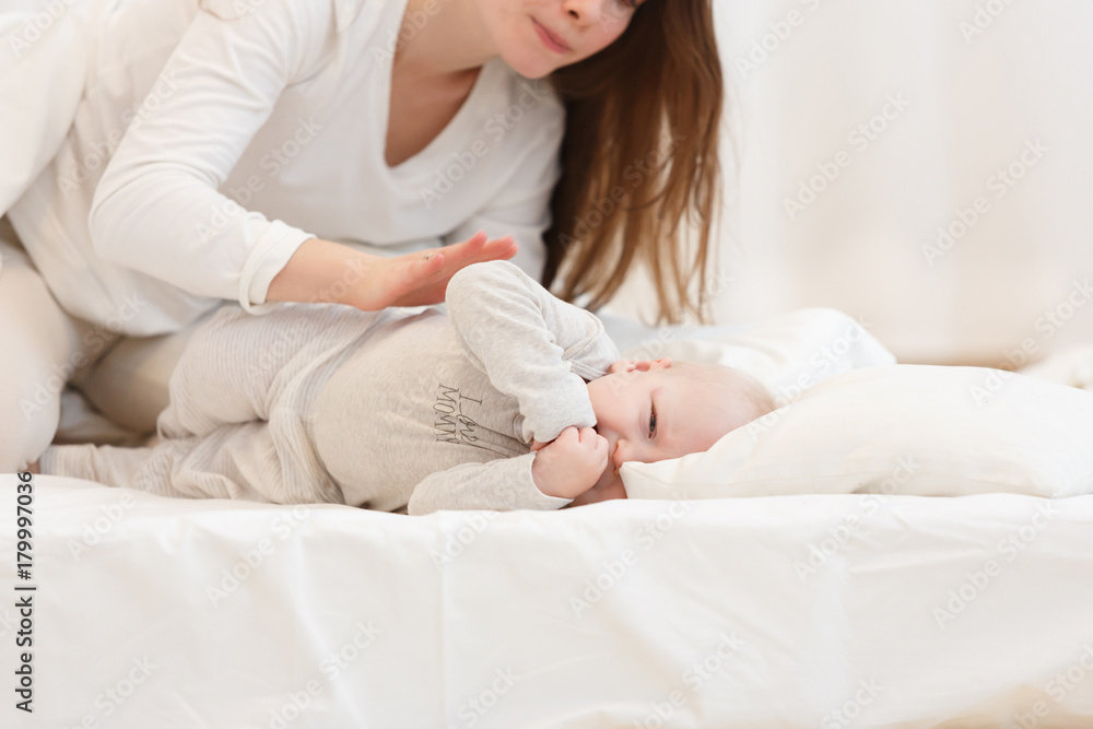 Portrait of young mother trying to calm little boy throwing hysterical tantrum in bed before bedtime. white clothes, light house interior of a bedroom. Portrait of young mother trying to calm little boy throwing hysterical tantrum in bed before bedtime. white clothes, light house interior of a bedroom.