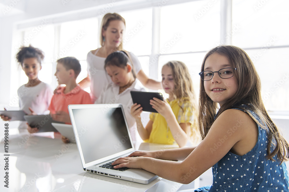 child with technology tablet and laptop computer in classroom teacher on the background