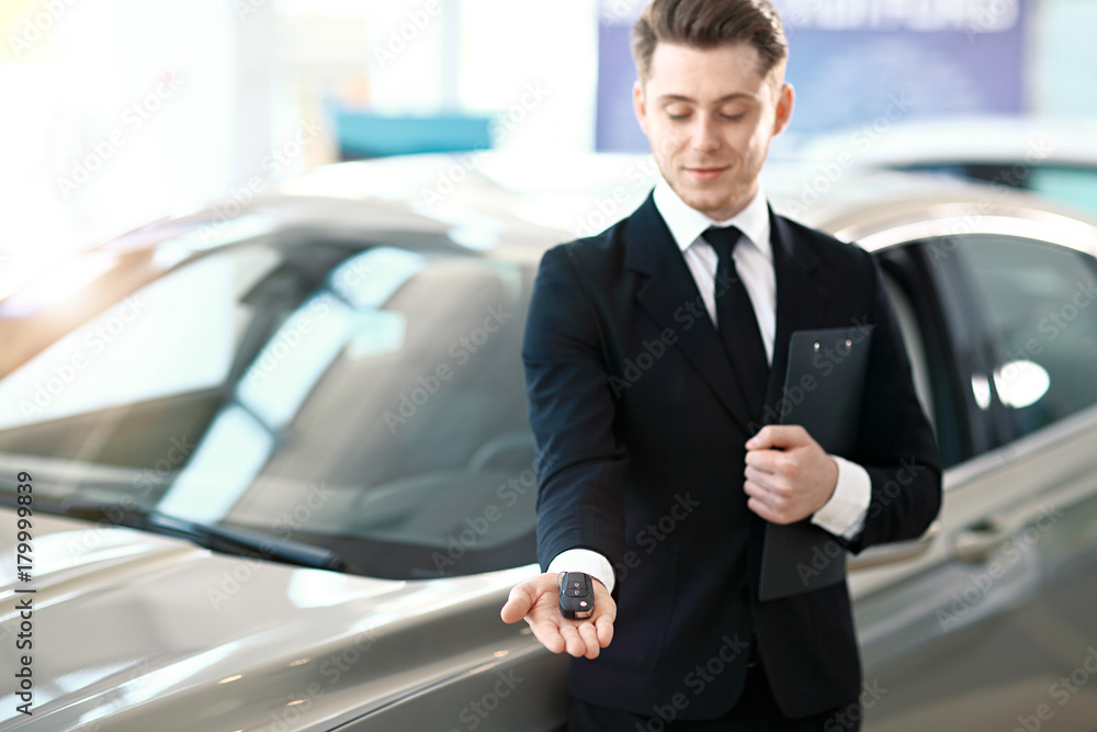 Handsome car dealer showing a car key. Focus on the key.