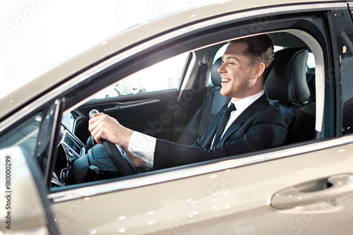 Formal wearing laughing young man behind the wheel.