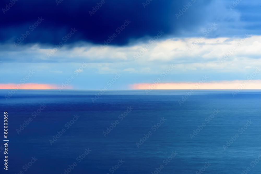 Stylized abstract landscape seascape sunset long exposure with clouds under different shades of blue, orange, yellow and red.