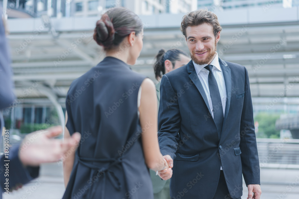 Businessman and businesswoman shaking hand and smiling after discuss new project success, supported by colleagues applauded in cityscape background Businessman and businesswoman shaking hand and smiling after discuss new project success, supported by colleagues applauded in cityscape background