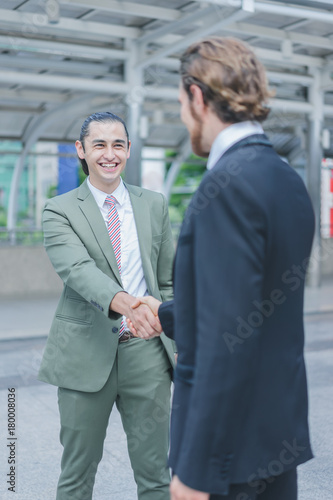 Profession two businessmen shaking hand and smiling after discuss new project success in cityscape background