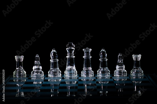 Glass Chess Set Standing on a Chessboard with a Dark Background, including the Rook, Knight, Bishop, Queen and King Pieces