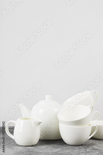 Clean white tableware (teapot, cups, saucers) on a gray background