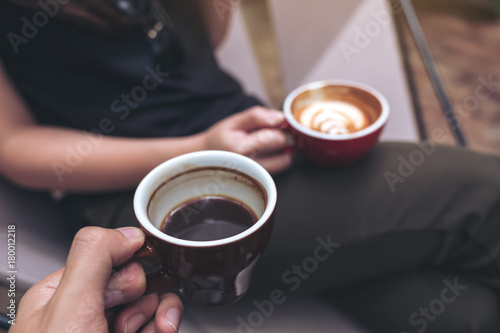 Closeup image of two people sitting and holding coffee cups in modern cafe