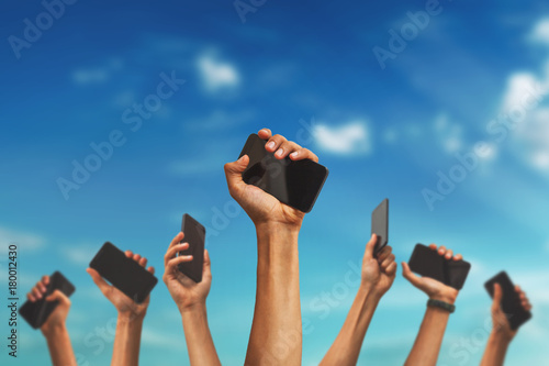 group of people's hands holding phones and rising them up against sky
