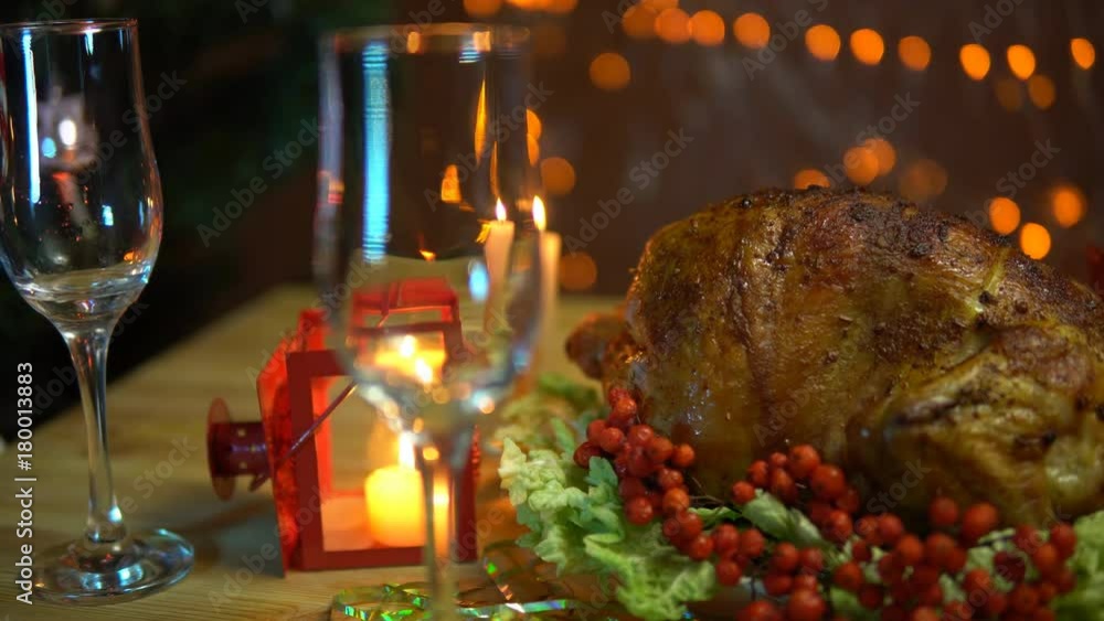 In the glass pour champagne next to the fried bird on a plate with a salad on the table on a background of yellow electric lights with a festive Christmas dinner in the evenings. In the glass pour champagne next to the fried bird on a plate with a salad on the table on a background of yellow electric lights with a festive Christmas dinner in the evenings.