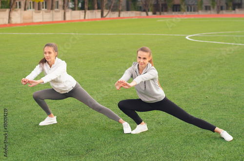 Two athletic girls stretching legs before doing exercises. Sport and training. Sport tight clothes. Sporty girls. Fitness concepts. Outdoor