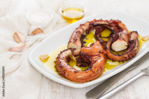 grilled octopus with garlic on white dish on wooden background