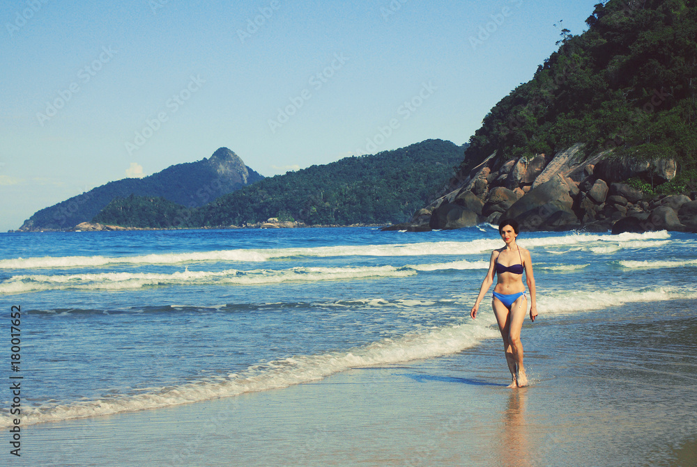 mid age woman in swimsuit walking along the seashore, Brazil