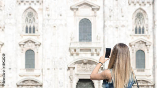 Pretty tourist teenager taking a photo with her mobile phone in Duomo square, the main landmark of Milan, Italy