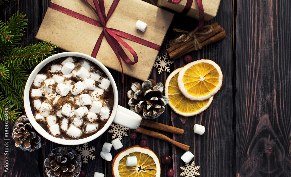 A cup of hot coffee with marshmallow, spruce branches, cones, Christmas gifts, mugs of orange, snowflakes, cinnamon. Traditional festive decoration Christmas dark background top view. A cup of hot coffee with marshmallow, spruce branches, cones, Christmas gifts, mugs of orange, snowflakes, cinnamon. Traditional festive decoration Christmas dark background top view.