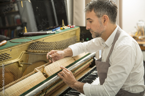 Technician tuning a upright piano using lever and tools