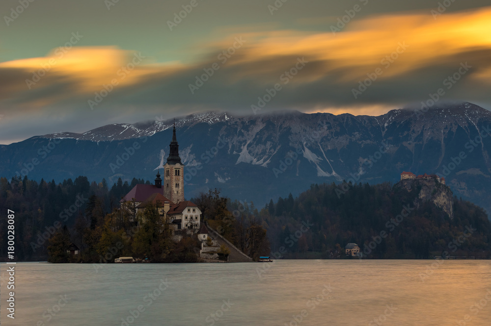 Bled, Slovenia - Beautiful autumn sunset at Lake Bled with the famous Pilgrimage Church of the Assumption of Maria with Bled Castle and Julian Alps at background. Moving clouds above the Alps