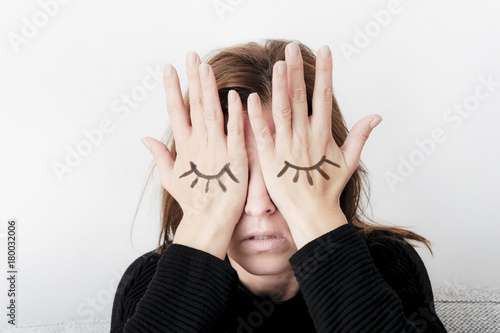 Young woman is covering her eyes with her palms. Eyes painted on her hand. Sorrow concept.