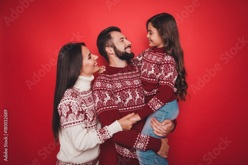 Holly molly noel x mas time! Three relatives bonding, married couple of brunet and brunette, excited small girl, in knitted cute traditional costumes, jeans, embracing