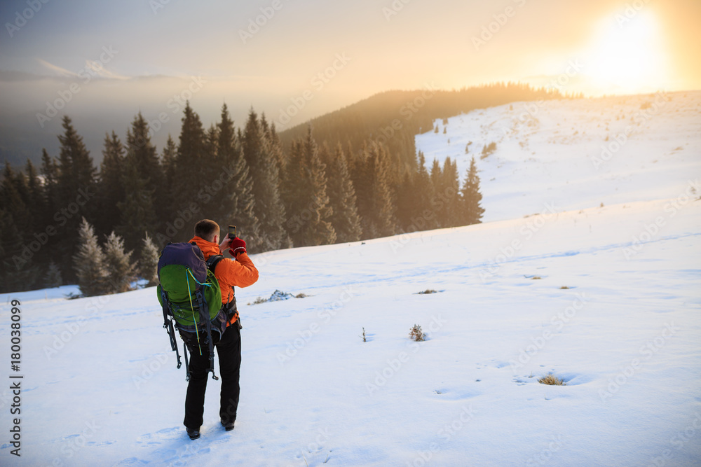 Hiker in winter mountains. Young man has a rest in mountains. Man with backpack trekking in mountains. Winter hiking. Beautiful sunrise in the winter mountains