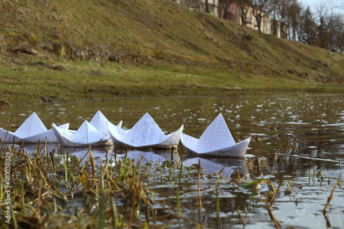 Origami paper ships sailing in river. Paper boats made from mathematics notebook paper.