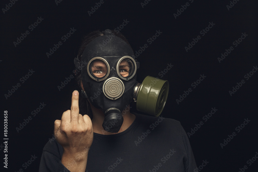 Portrait of man in gas mask on dark background, shows middle fingers sign by one hands Portrait of man in gas mask on dark background, shows middle fingers sign by one hands