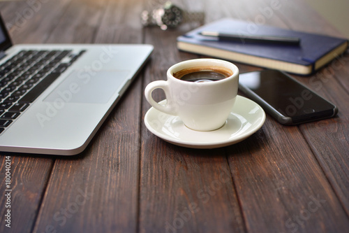 Cup of coffee on a office table near the laptop, phone and office chancery