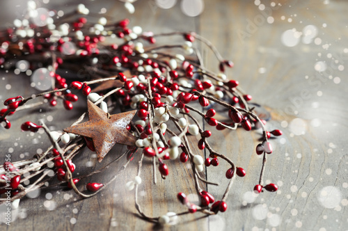 Christmas wreath with red and white berries and rusty metal stars on wooden background. Falling snow effect. Vintage Style. Copy space.