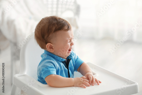 Cute little crying baby sitting on chair indoors