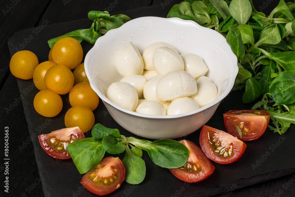 Mozzarella in bowl, tomatoes and different salad leaves