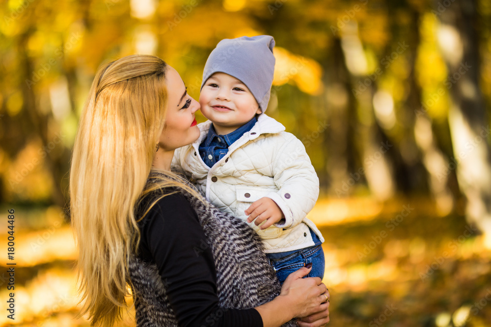 Mom and her son are in the autumn park, the son loves looking at his mother, the woman is holding his hands, in the background yellow leaves, the family spends the weekend in the park Mom and her son are in the autumn park, the son loves looking at his mother, the woman is holding his hands, in the background yellow leaves, the family spends the weekend in the park