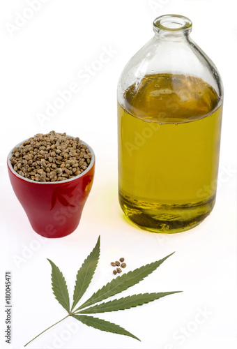 Hemp oil in a bottle with a seeds of cannabis in a red cup and a leaf of marijuana isolated on a white background.
