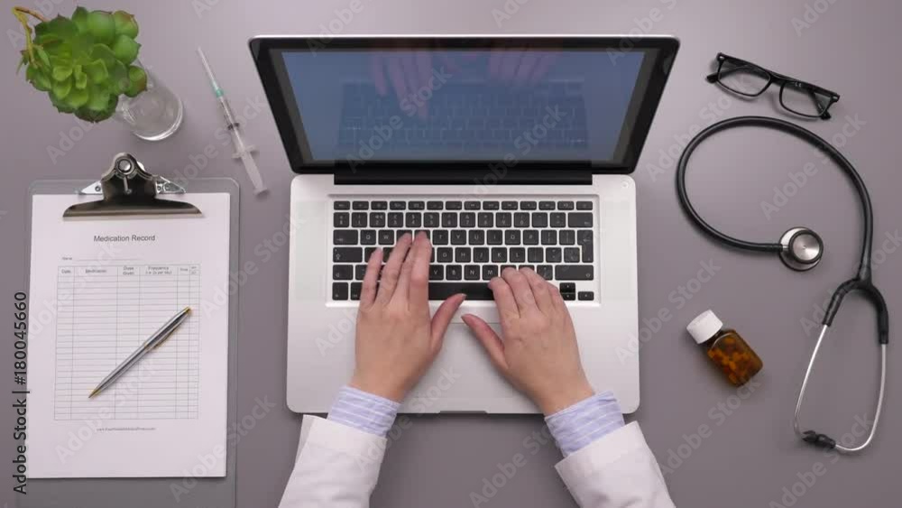 Overhead Shot Of Doctor Using Laptop While Writing On Report Overhead Shot Of Doctor Using Laptop While Writing On Report