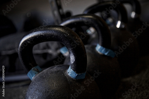 Gritty close-up of a row of heavy black kettlebells marked with blue on a gym floor