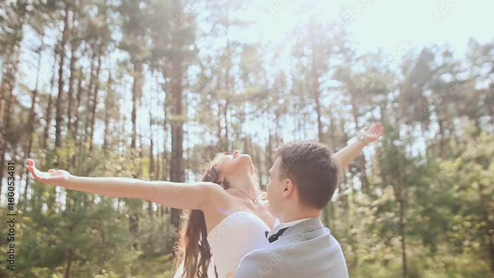 The bride and groom are posing in the forest. The young groom joyfully lifts the bride and circles her in the rays of sunlight. Beautiful background. Happy moment of a loving couple. Summer. Wedding The bride and groom are posing in the forest. The young groom joyfully lifts the bride and circles her in the rays of sunlight. Beautiful background. Happy moment of a loving couple. Summer. Wedding