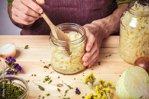 The cook puts sauerkraut in glass jars. On the table are spices, onions and cabbage. photo