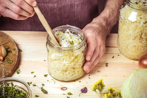 A bank of sauerkraut in the hands of a chef on the background of a table with ingredients. Process of starter